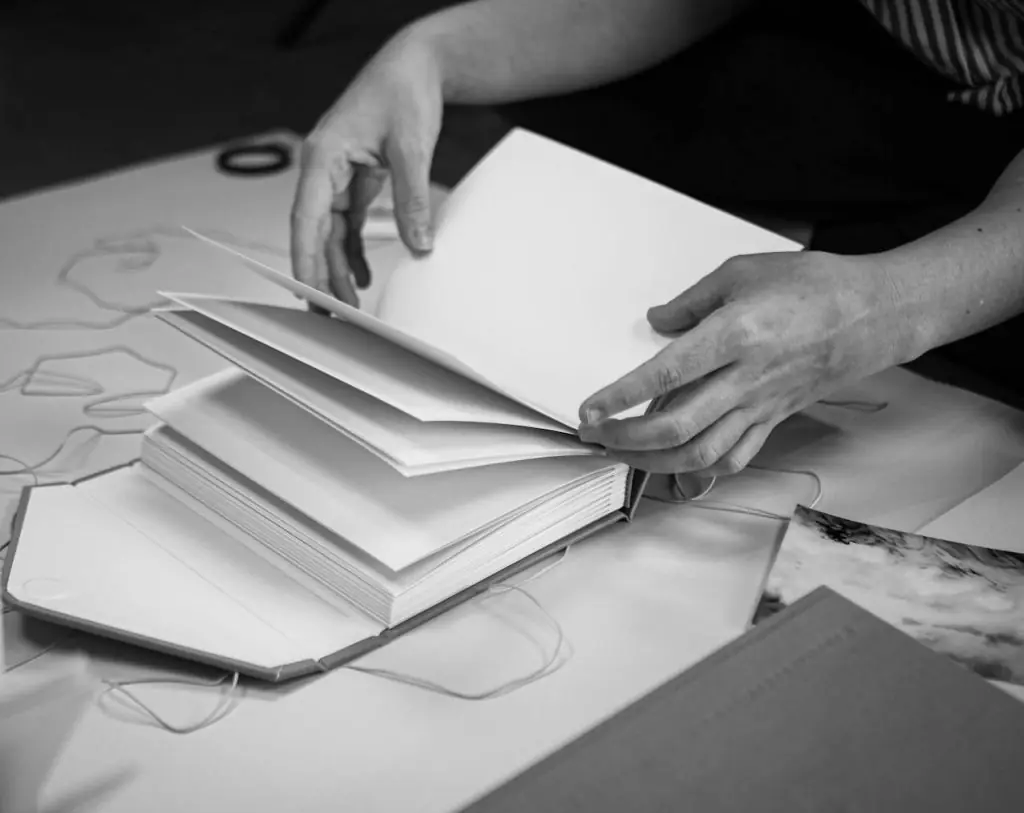 Close-up of hands flipping through blank pages of a book, in a black and white setting.